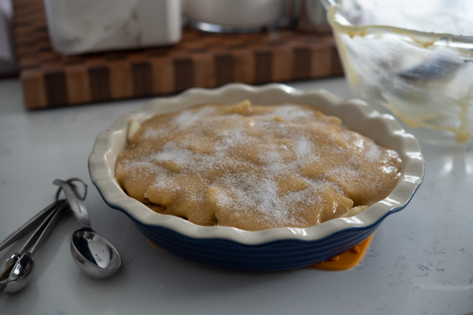 Granulated sugar is sprinkled on top of batter in a pie dish.
