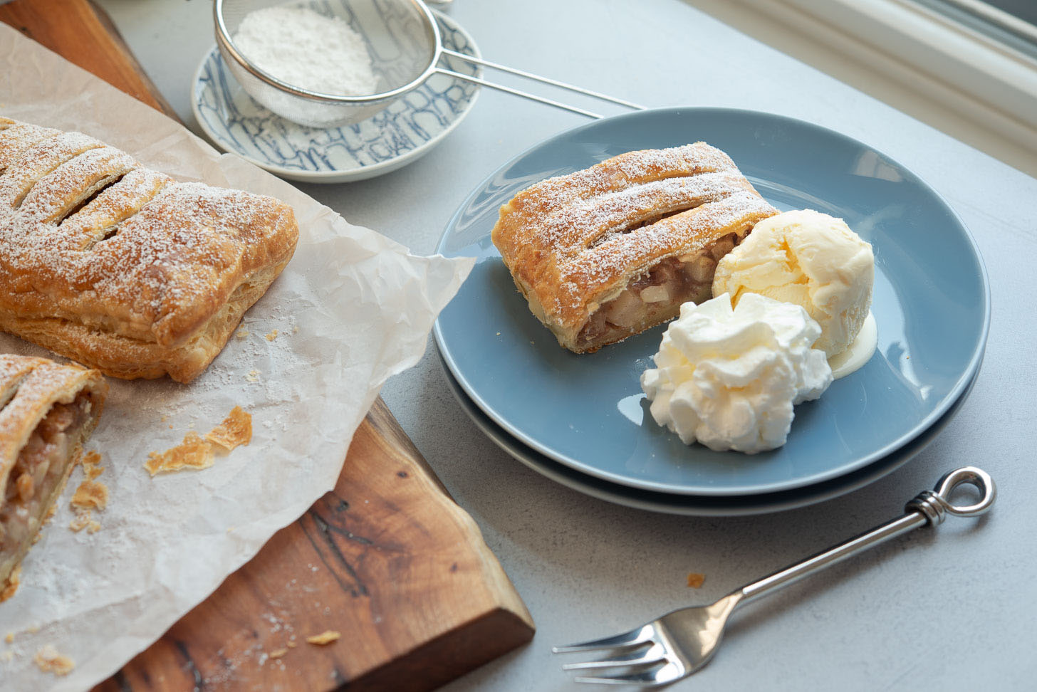 A slice of apple strudel with ice cream and whipped cream on a plate.