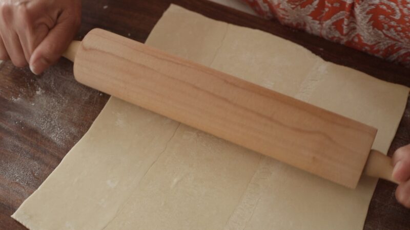 A rolling pin is stretching the puff pastry
