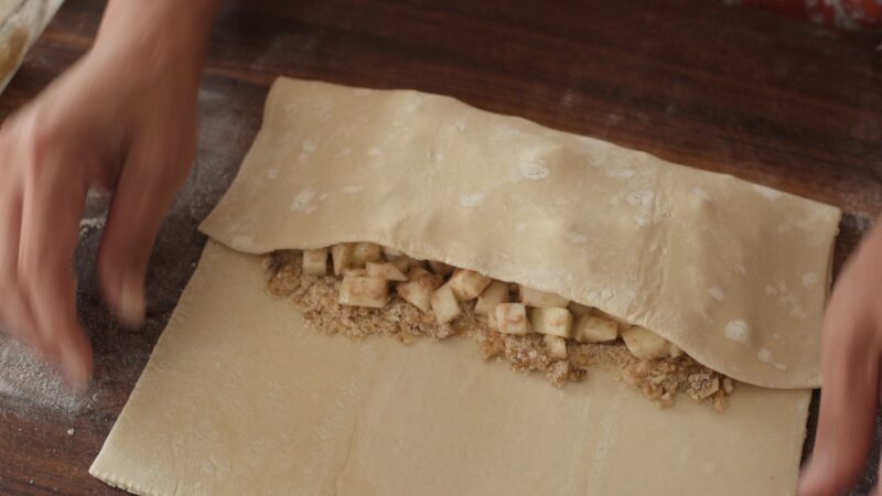 Forming a strudel with apple filling with puff pastry dough