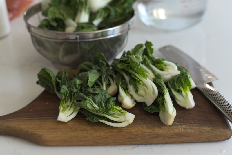 Baby bok choy is halved or quartered with a knife.