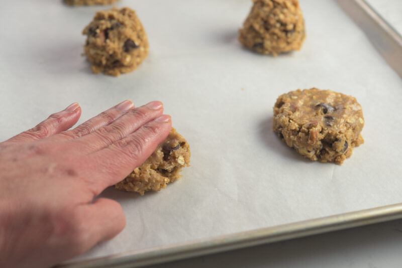 Cookie dough balls are being pressed by fingers on a cookie sheet.
