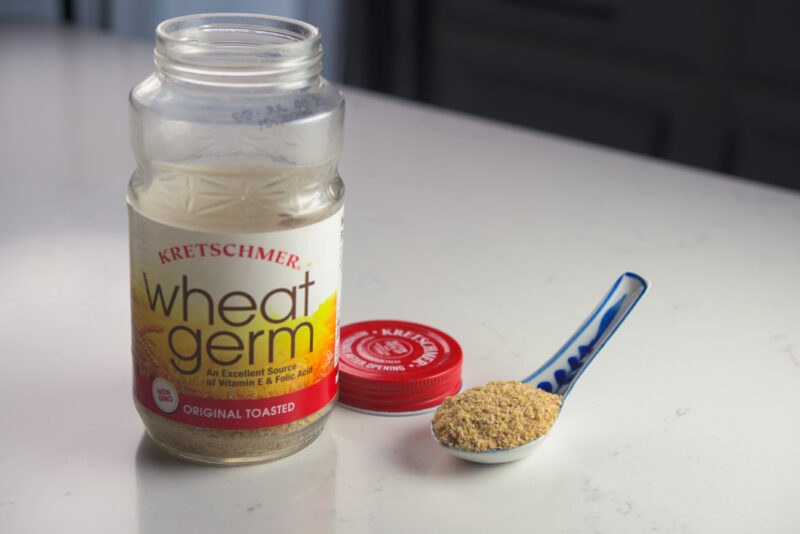 A spoonful of wheat germ is next to a jar of wheat germ.