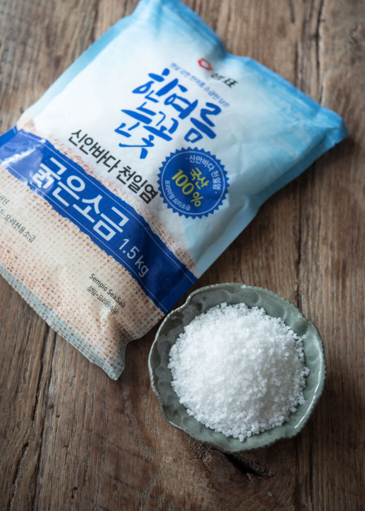 A packet and a bowl of Korean coarse sea salt are placed to show the salt crystals.