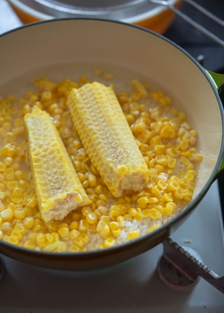 Rice, corn, and the cob are combined in a pot.