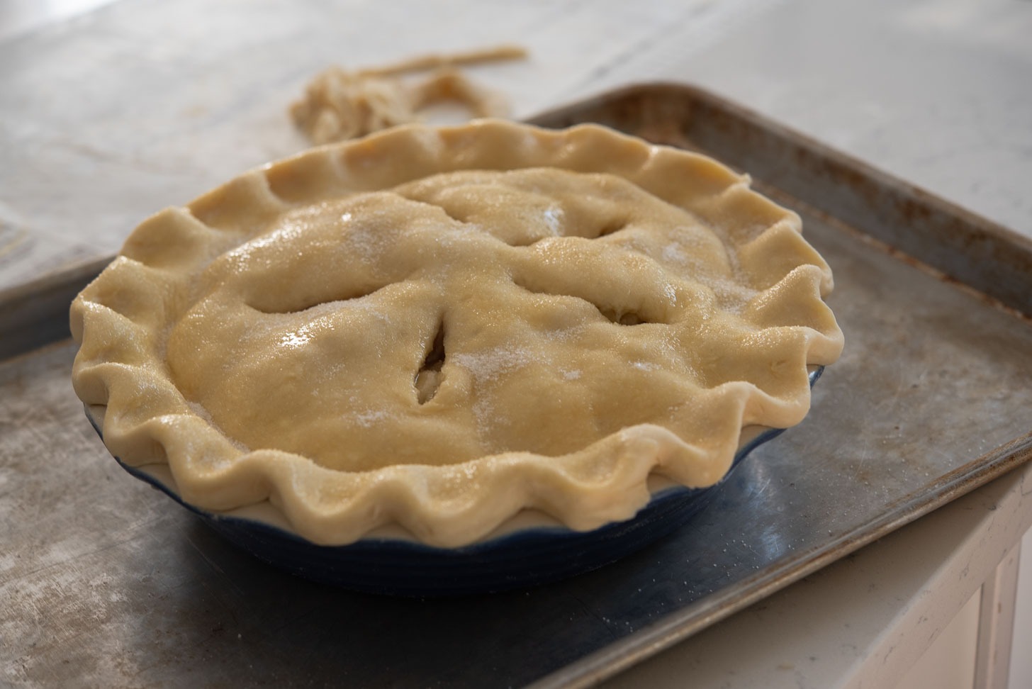 Sugar is sprinkled on the top of pie crust of an assembled apple pie.