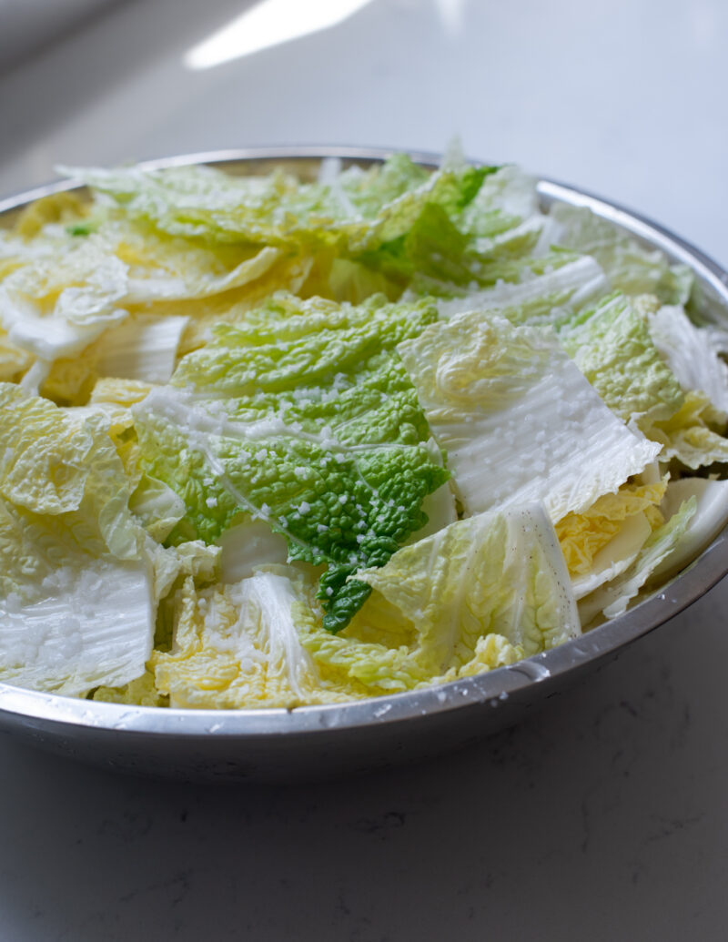 Cabbage pieces are sprinkled with coarse sea salt in a large mixing bowl.
