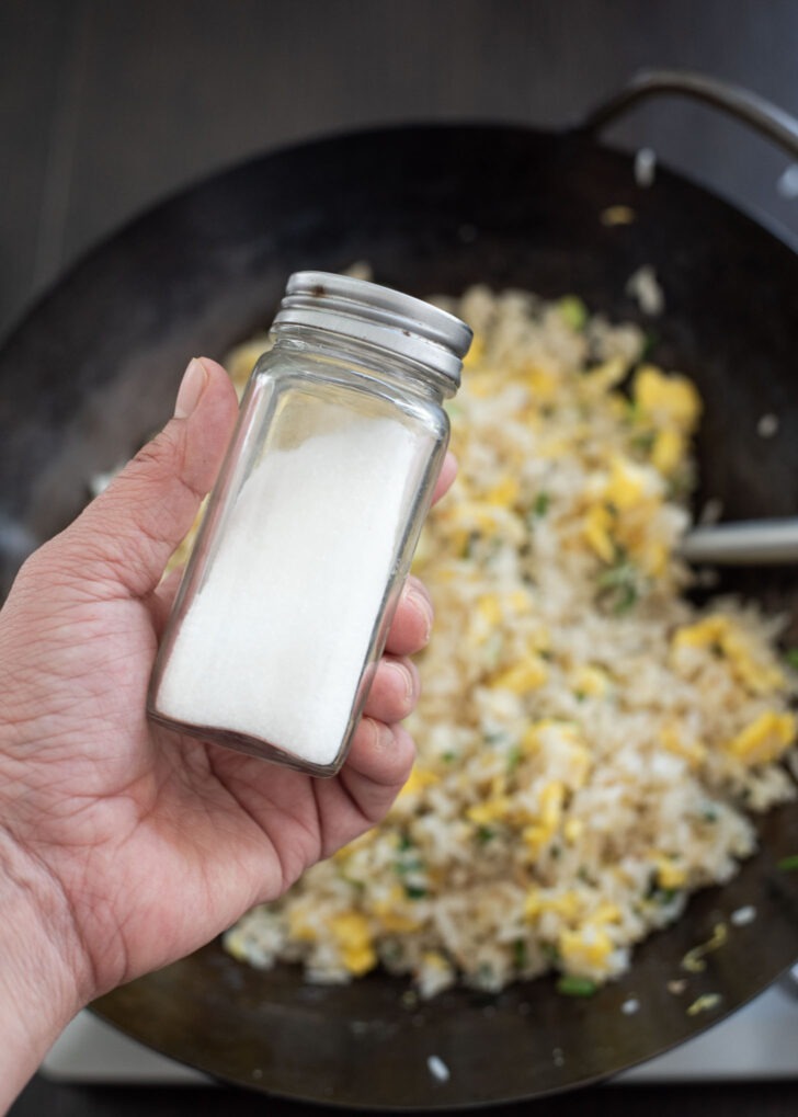 A tiny bit of MSG is added to egg fried rice in a wok.