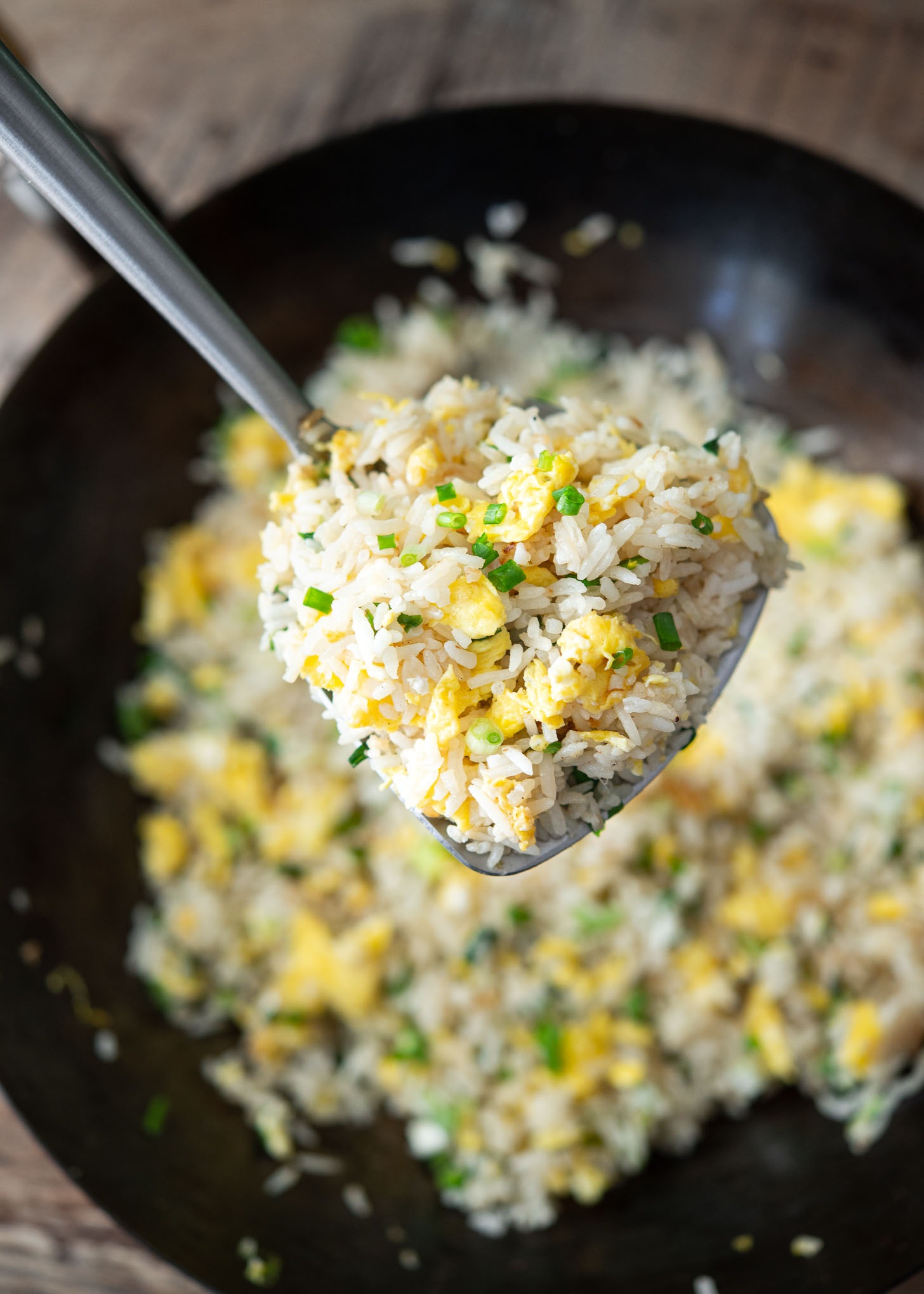 A spatula is holding up some of egg fried rice above the rest of fried rice.
