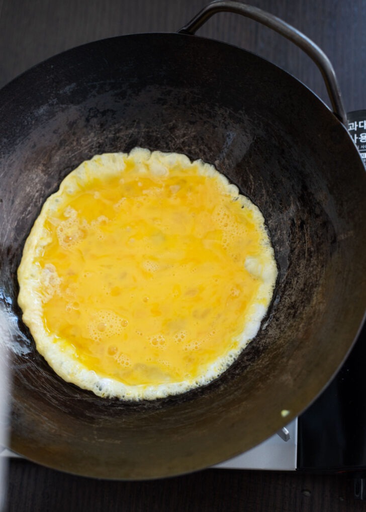 Beaten egg is added to the hot wok and bubbly on the edge.