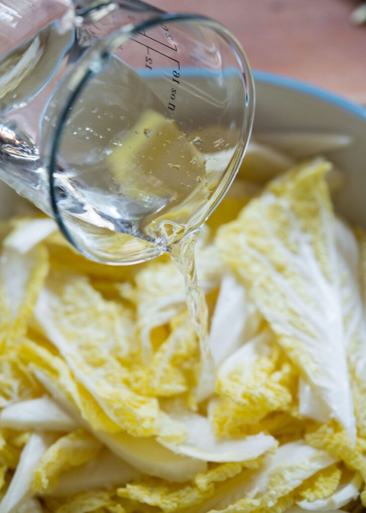 Water is drizzled over salted cabbage leaves.