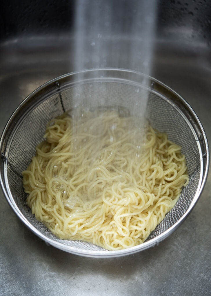 Cooked wheat noodles being rinsed under the cold water