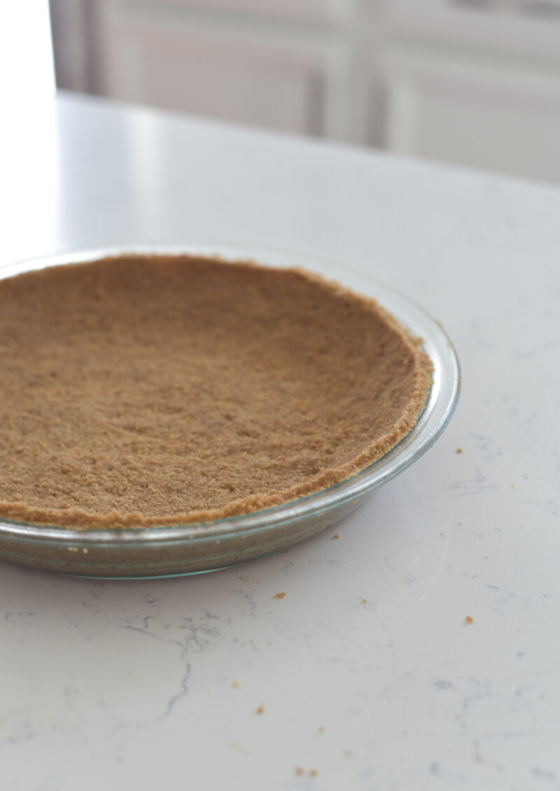 Graham cookie crumbs are pressed onto a pie dish.