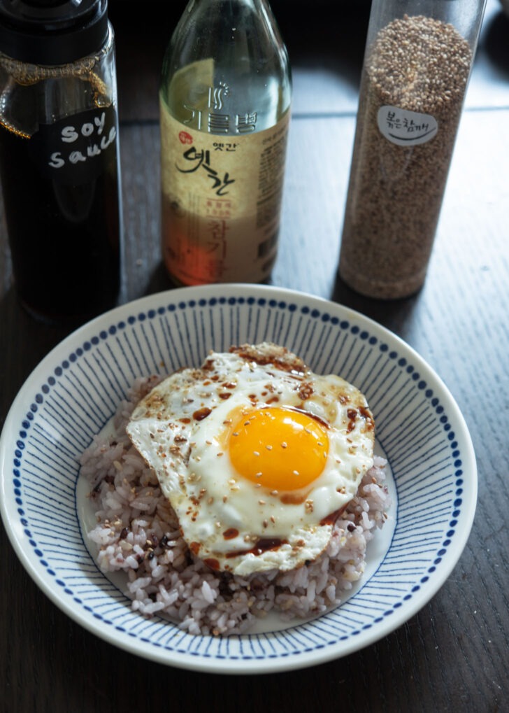 A fried egg with rice drizzled with soy sauce, sesame oil, and sesame seeds.