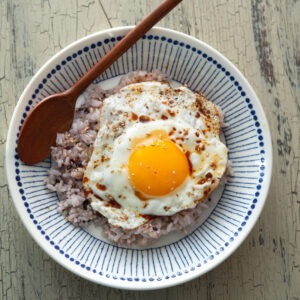 A bowl of gyeran bap is garnished with sesame seeds and served with a spoon.