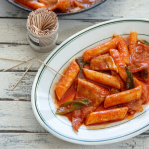 Spicy Korean rice cakes (tteokbokki) is made with gochujang and served on a platter with toothpicks.