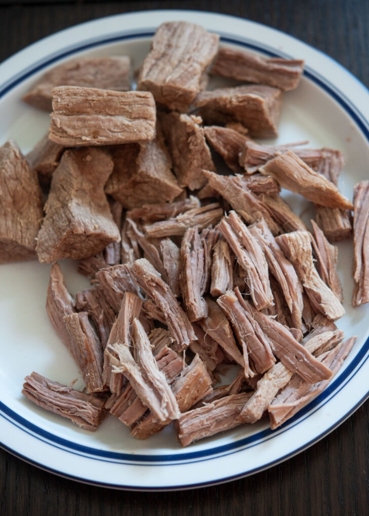 Shredding braised beef into bite size pieces.