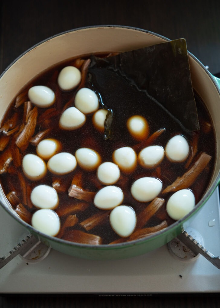 Mixing beef, quail eggs, and sea kelp with jangjorim broth in a pot.