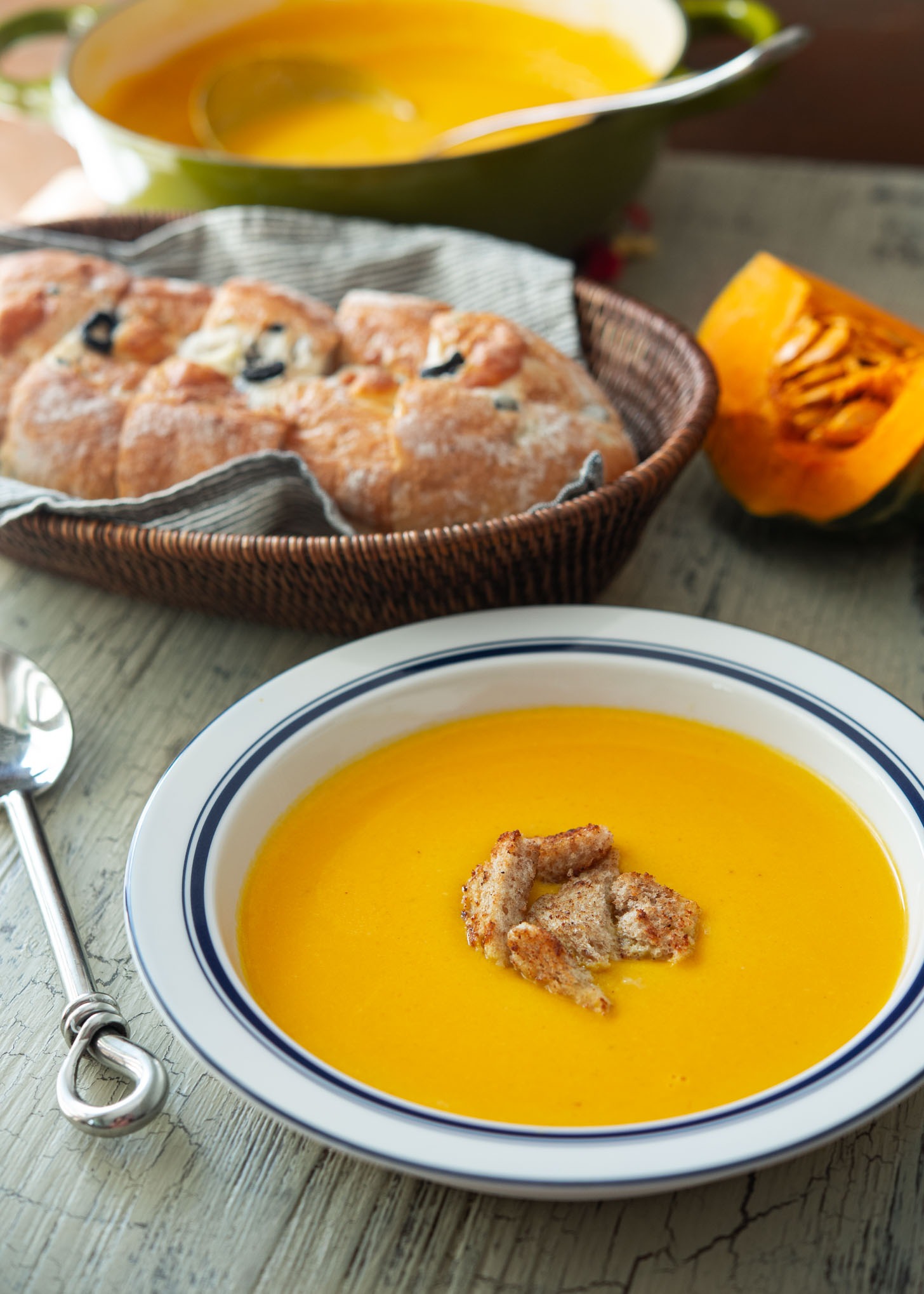 Kabocha squash soup in a serving bowl with crusty bread on the side.