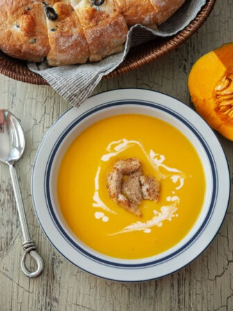 A bowl of kabocha squash soup garnished and served with crusty bread.