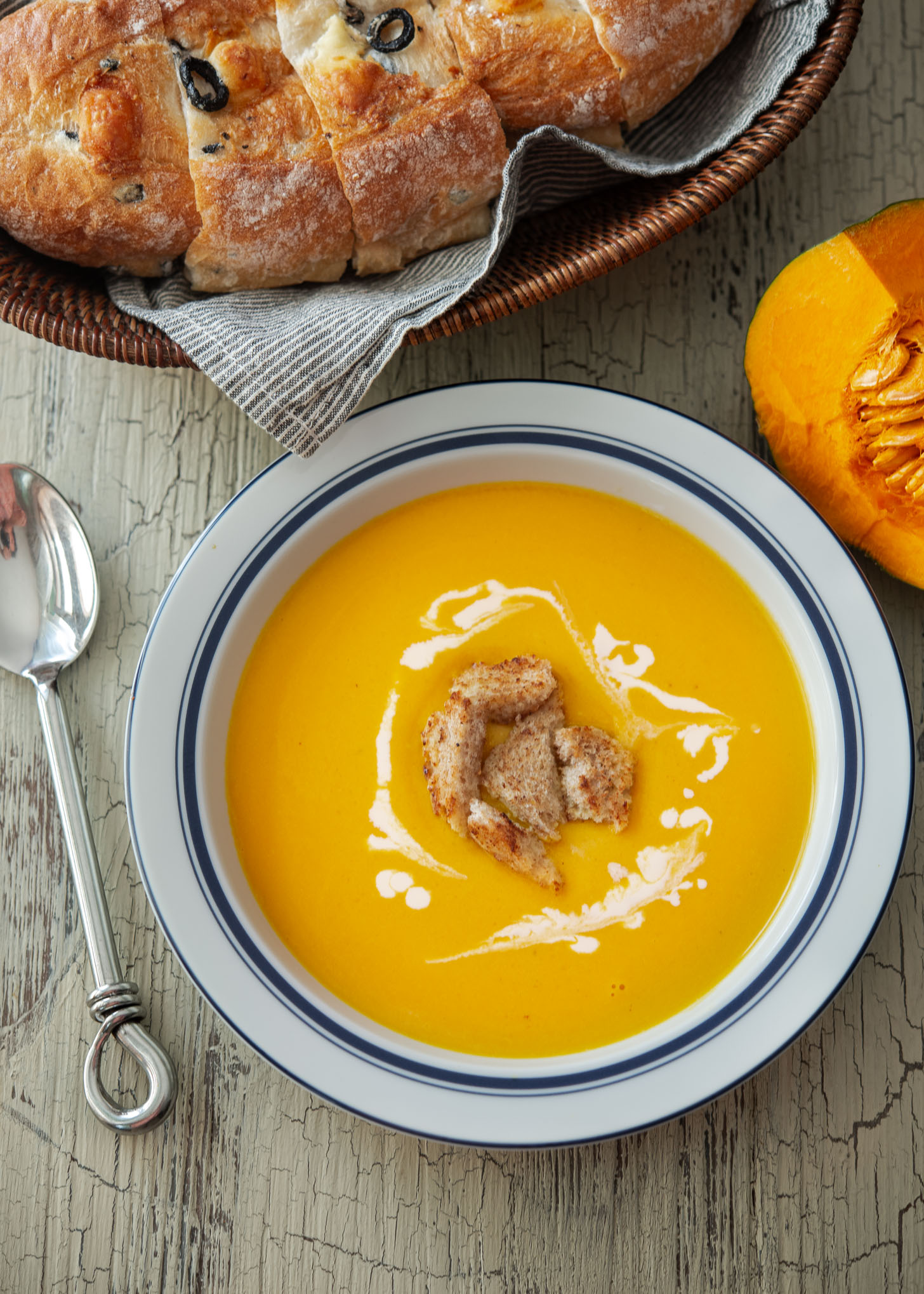 A bowl of kabocha squash soup garnished and served with crusty bread.