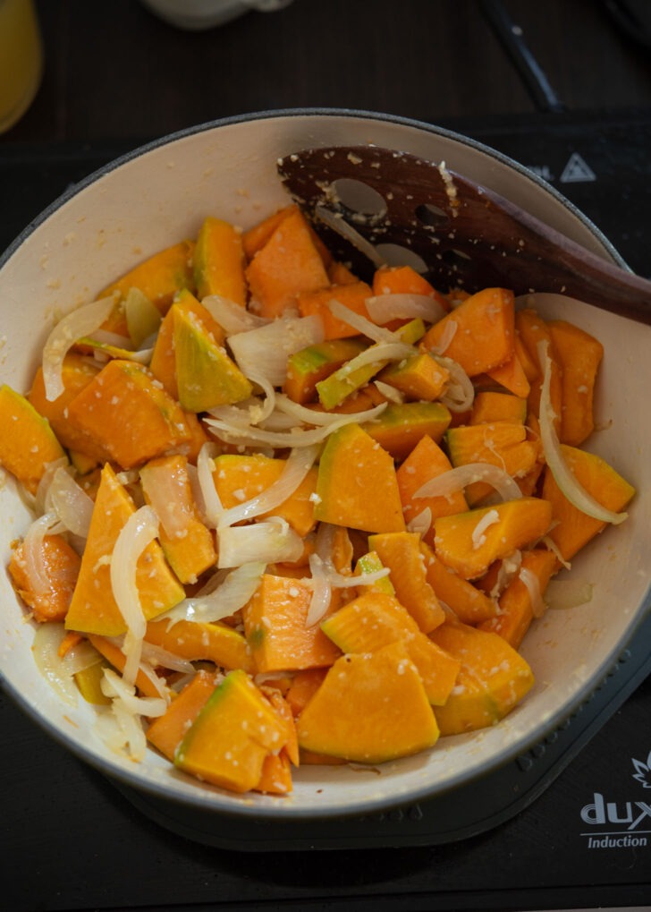 Kabocha squash pieces added to aromatic ingredients in a pot.