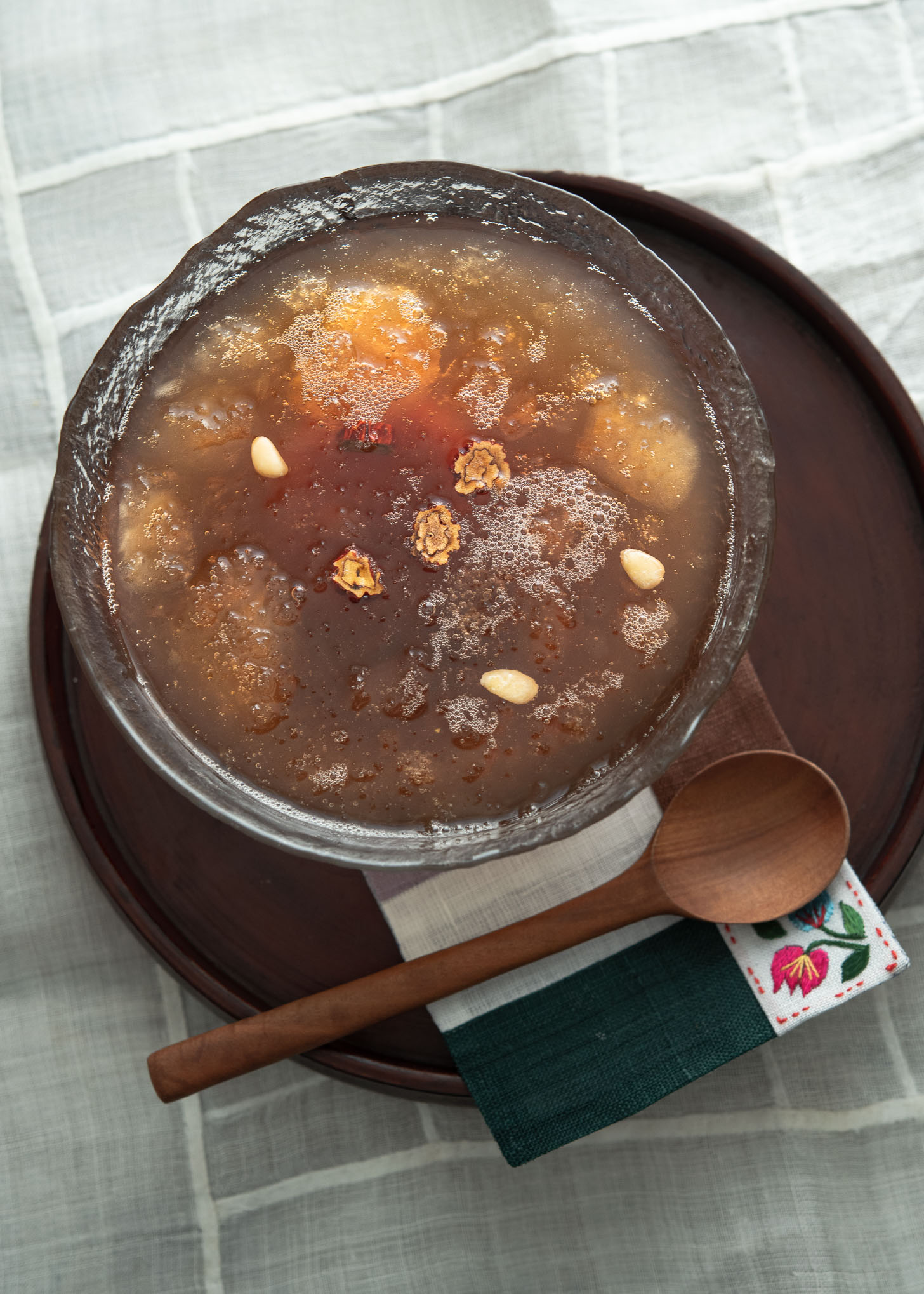 A bowl of Sujenggwa is garnished with pine nuts and jujube and served with a spoon on the side.