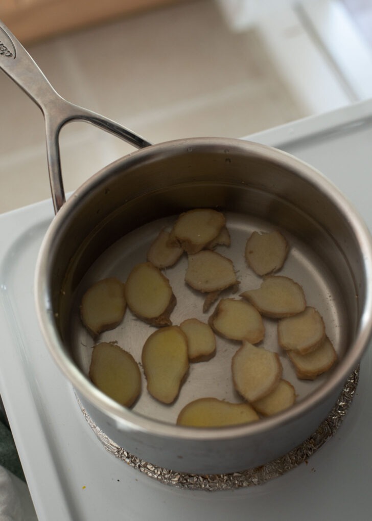 A bunch of ginger slices are simmering in a pot of water.