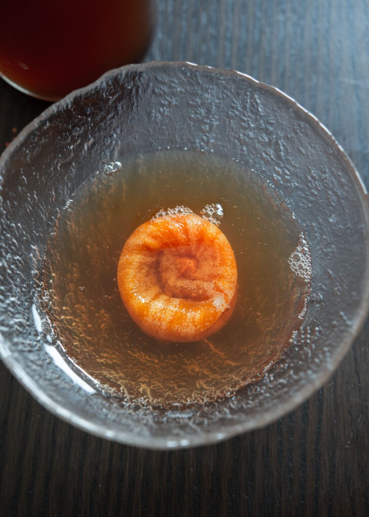 Flattened dried persimmon is soaking in Korean cinnamon punch in a bowl.