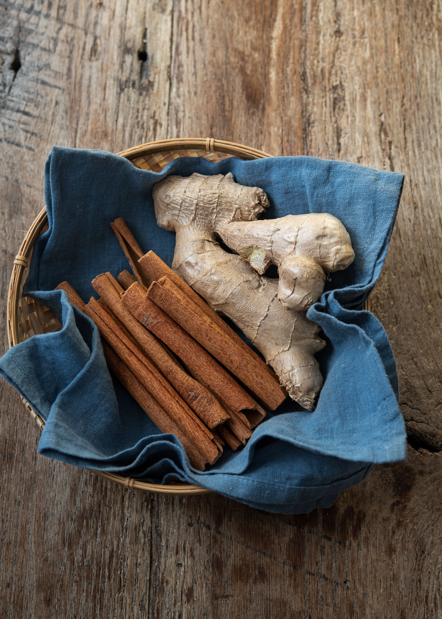 Cinnamon sticks and ginger are in a basket line with a blue napkin.