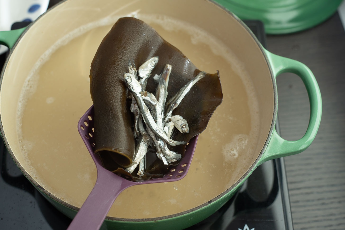 Anchovies and sea kelp is removed from a pot of anchovy stock.