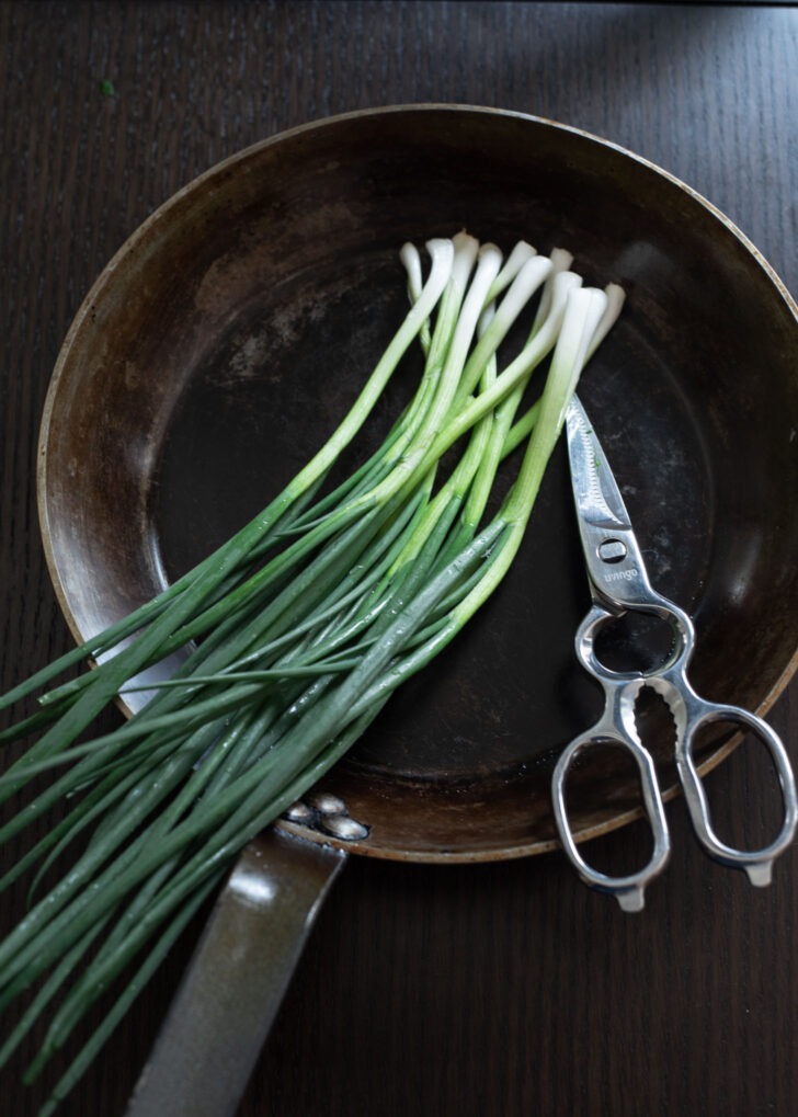 A bunch of scallion (or green onion) placed on a skillet with a pair of scissor.