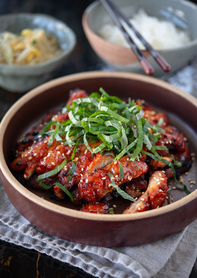 Red chicken bulgogi (Korean bbq chicken) garnished with shredded perilla leaves and sesame seeds.