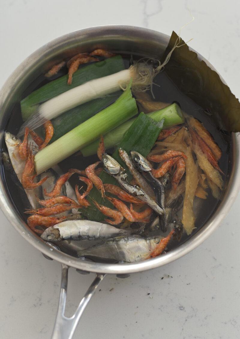 Various dried seafood and leek are combined with water in a pan.
