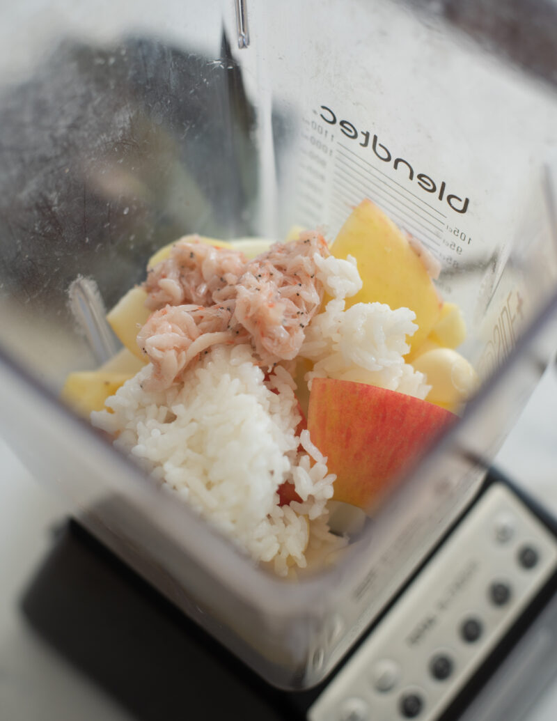 A blender filled with apple, onion, cooked rice, and salted shrimp.