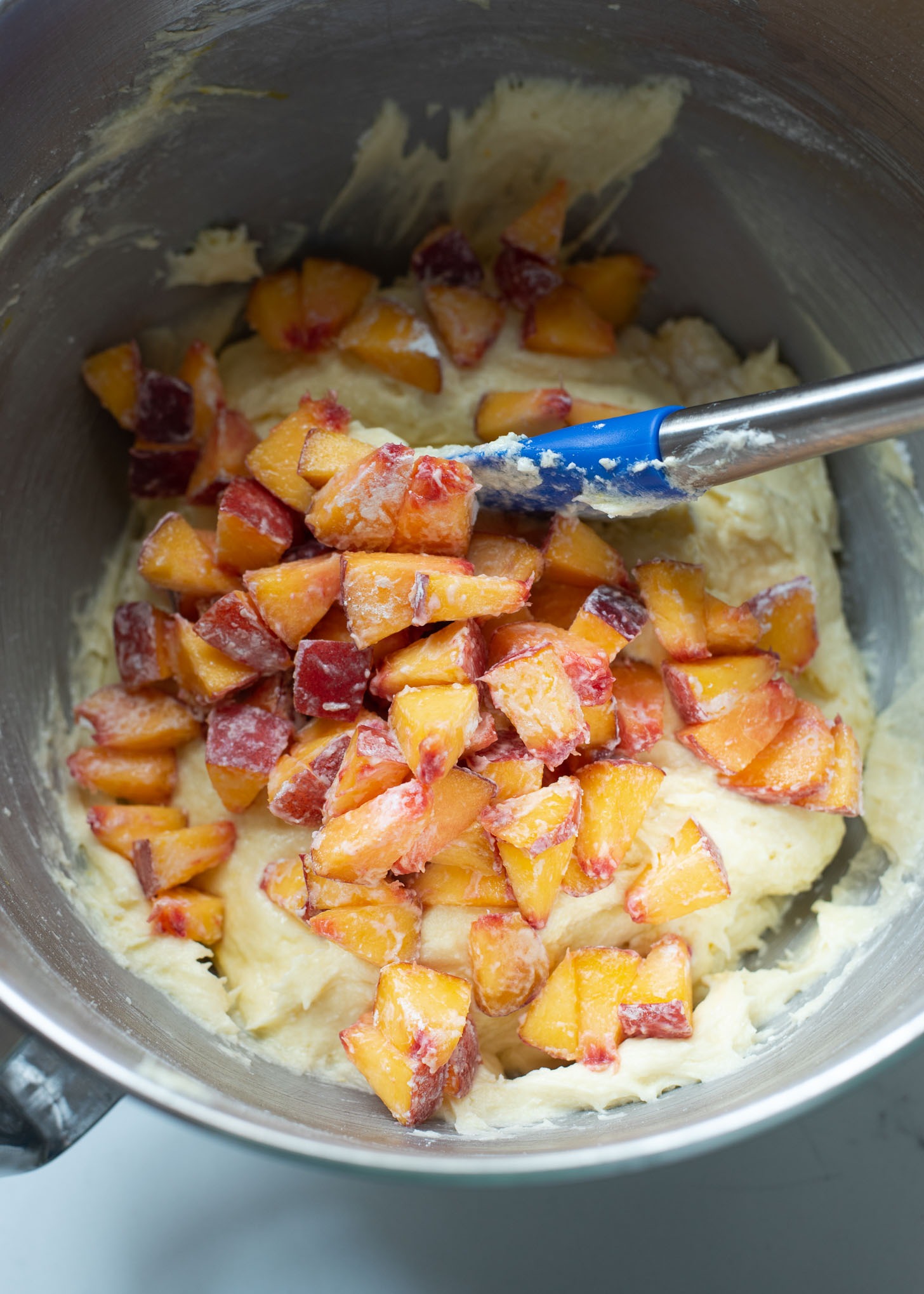 Diced peach slices coated with flour are added to peach pound cake batter in a mixer.