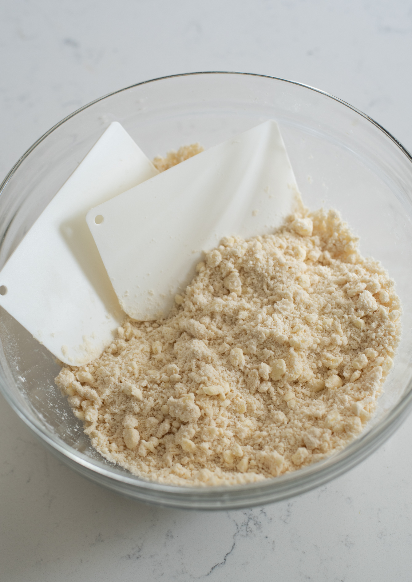 Pie crust dough is blended to coarse crumb mixture using dough scrapers.