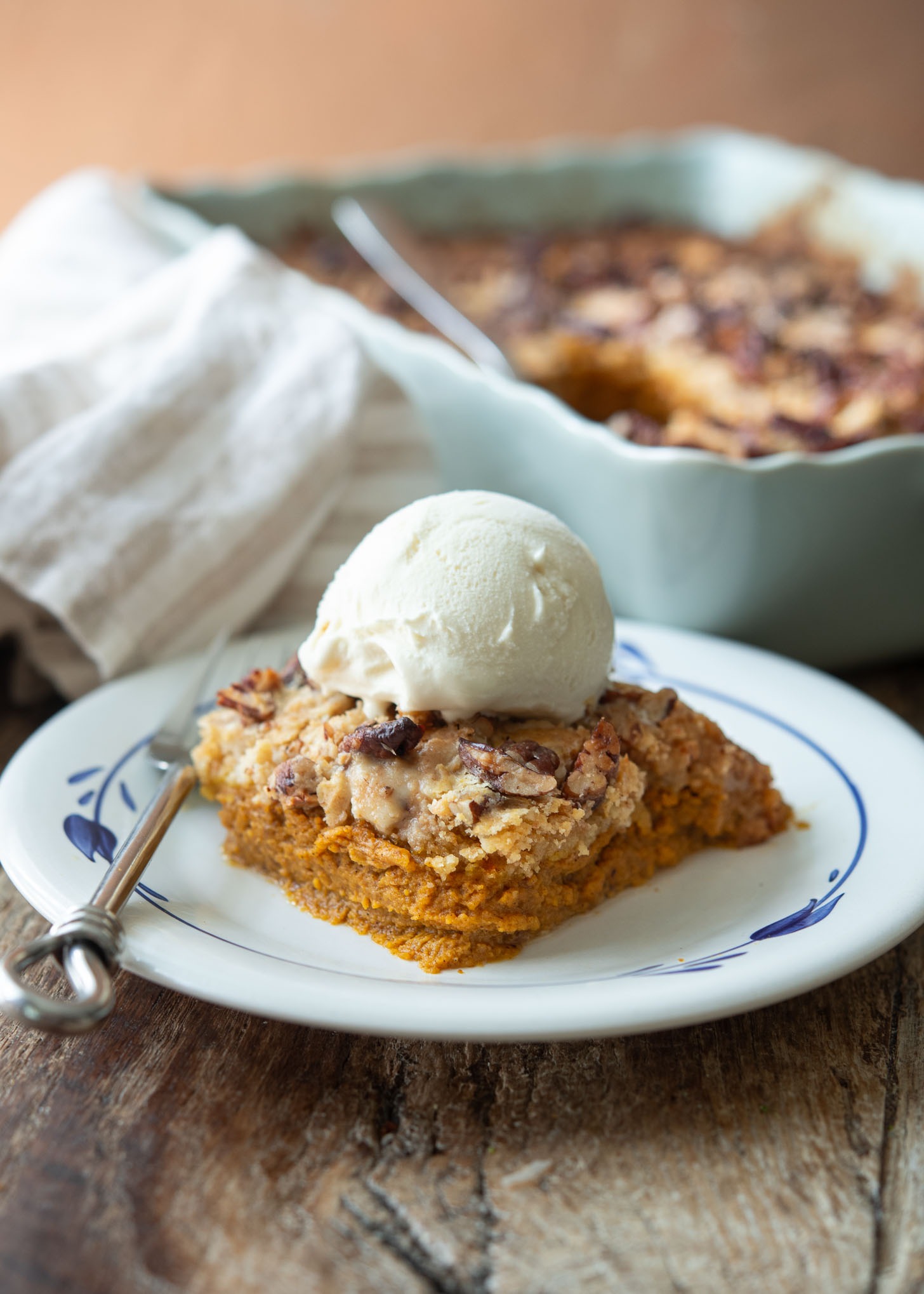 A slice of pumpkin pie crunch topped with ice cream on a dessert plate.