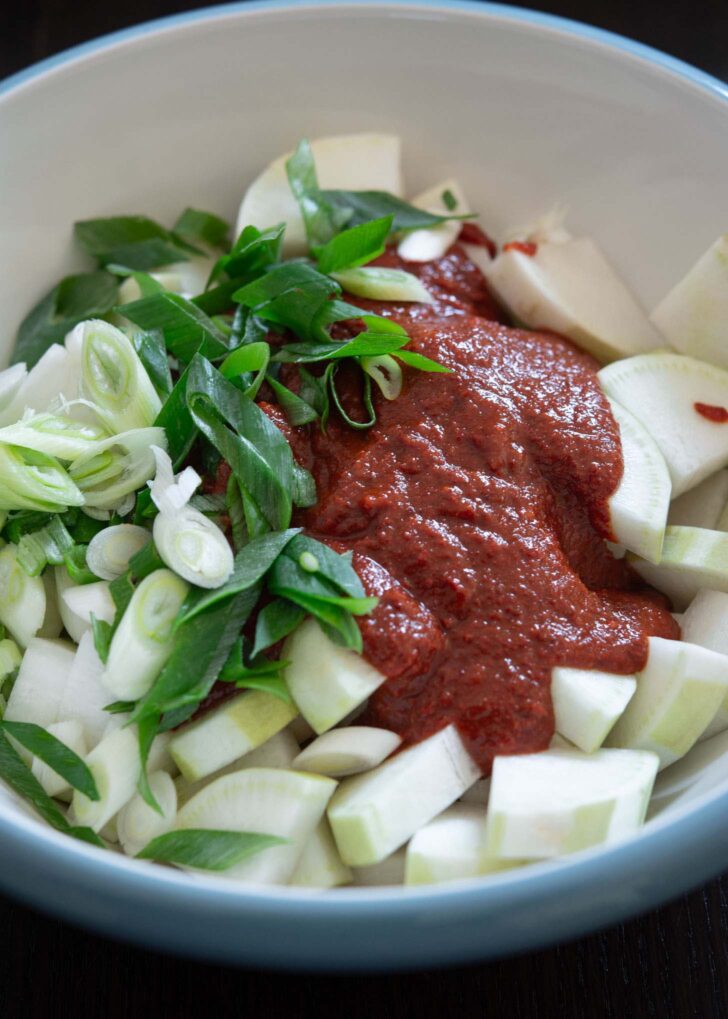 Sliced radish, green onion, kimchi seasoning combined in a mixing bowl.