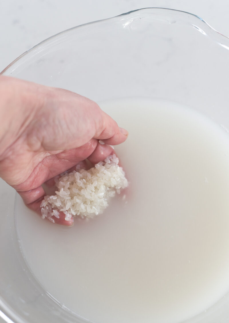 A hand is rinsing rice with water in a bowl.