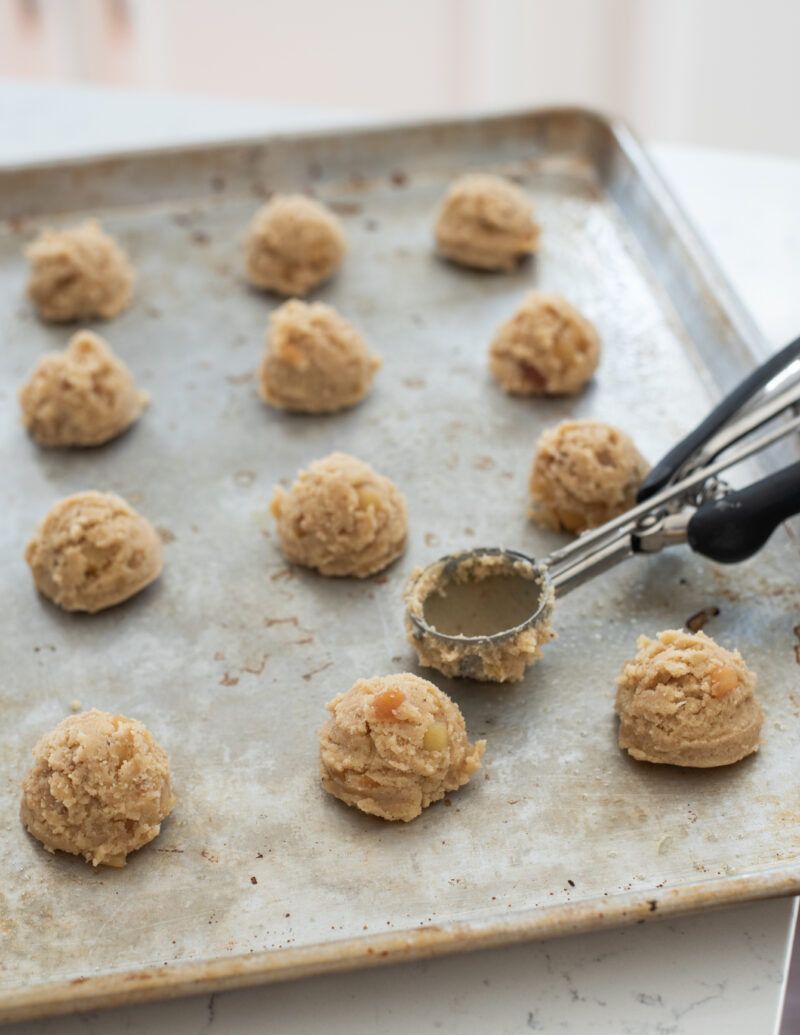 Apple cooki dough is scooped out into balls with a cookie scoop on a cookie sheet .