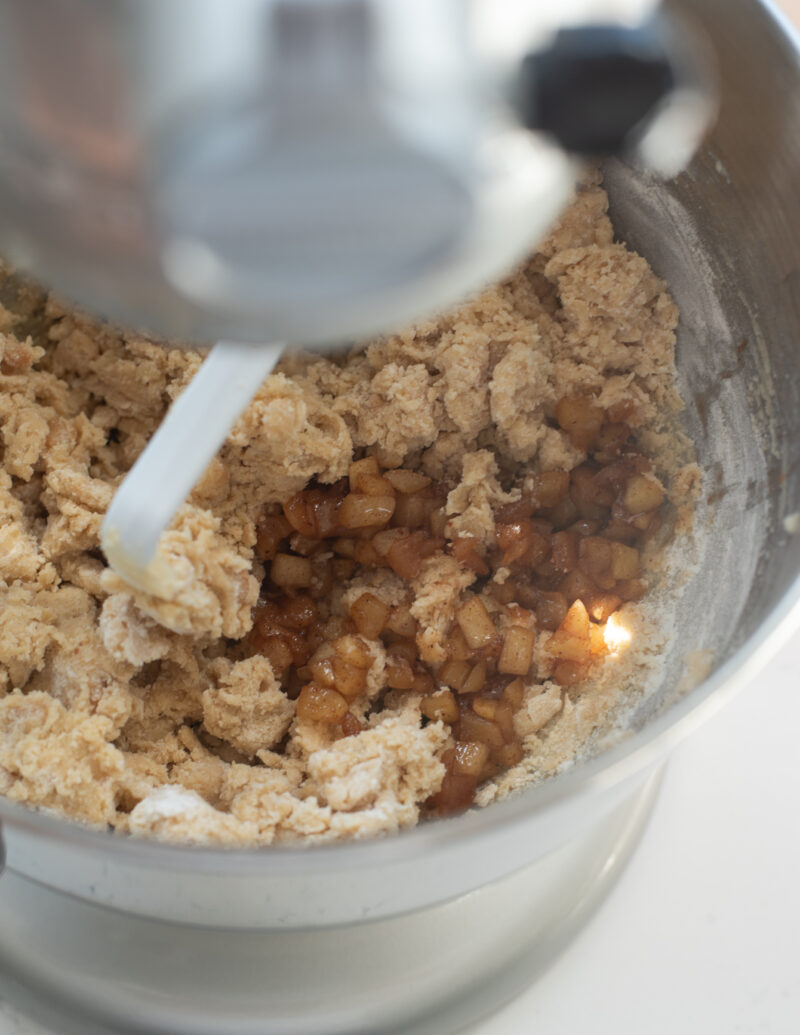 Cooked apple is added to the cookie dough in a stand mixer.