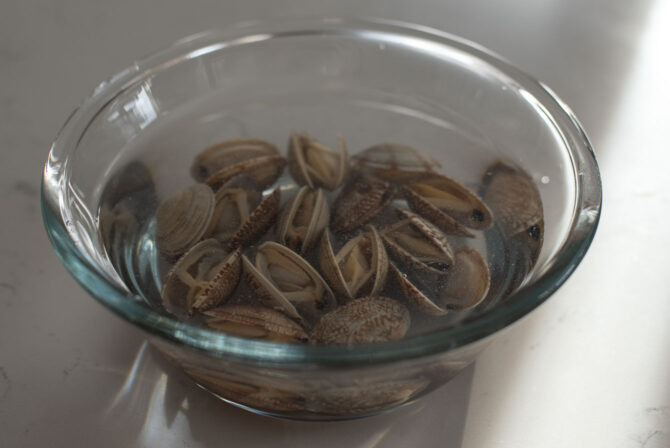 Frozen clams thawing in the cold water in a bowl.