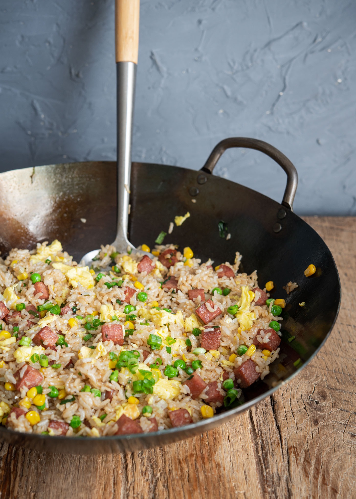 Fried rice is made with spam, peas, and corn with day-old rice in a wok.