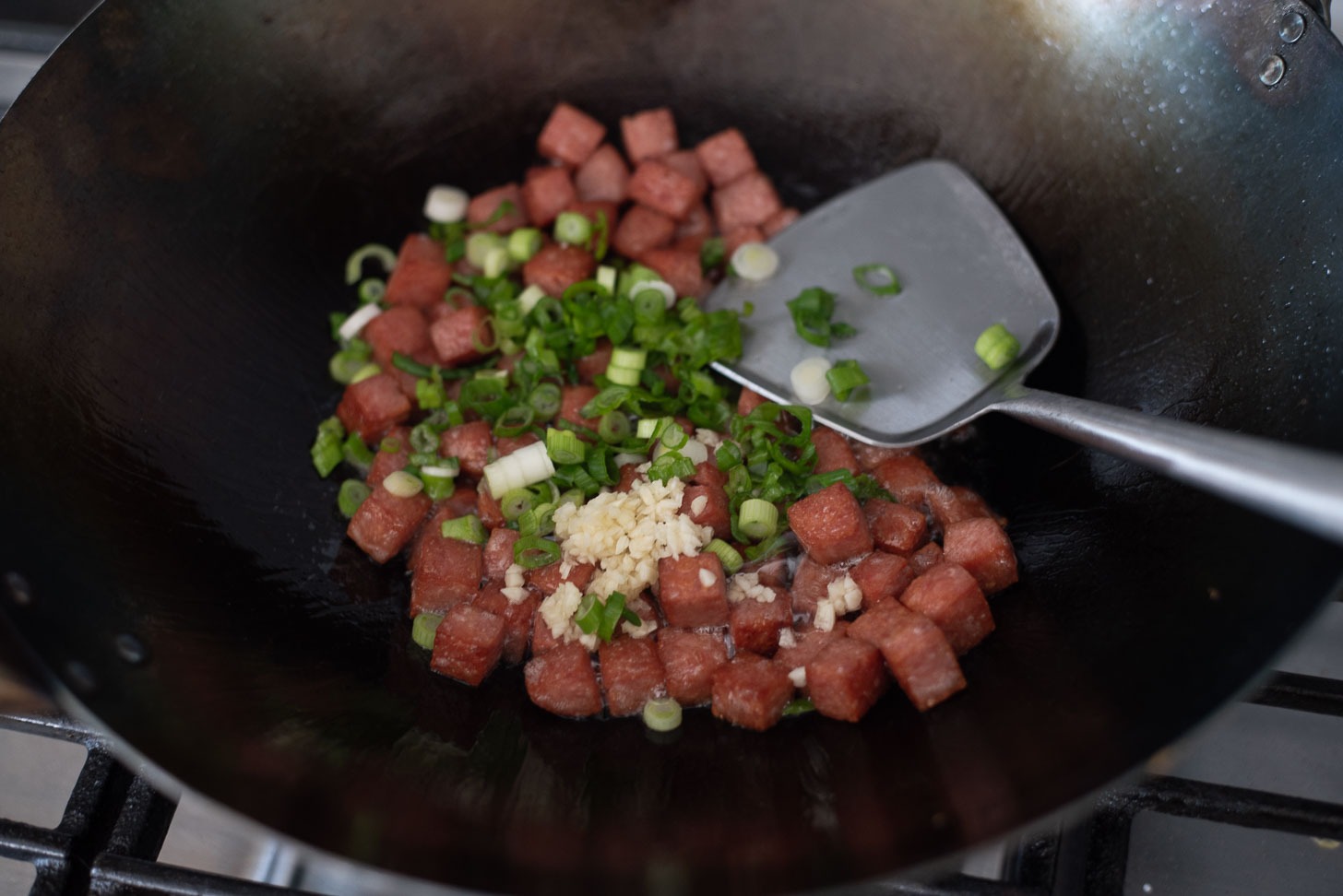 Green onion and garlic is added to fried Spam pieces.