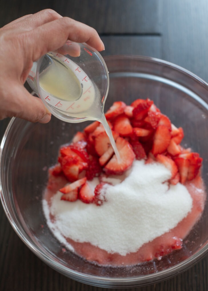Crushed strawberries combined with sugar and lemon juice in a mixing bowl.