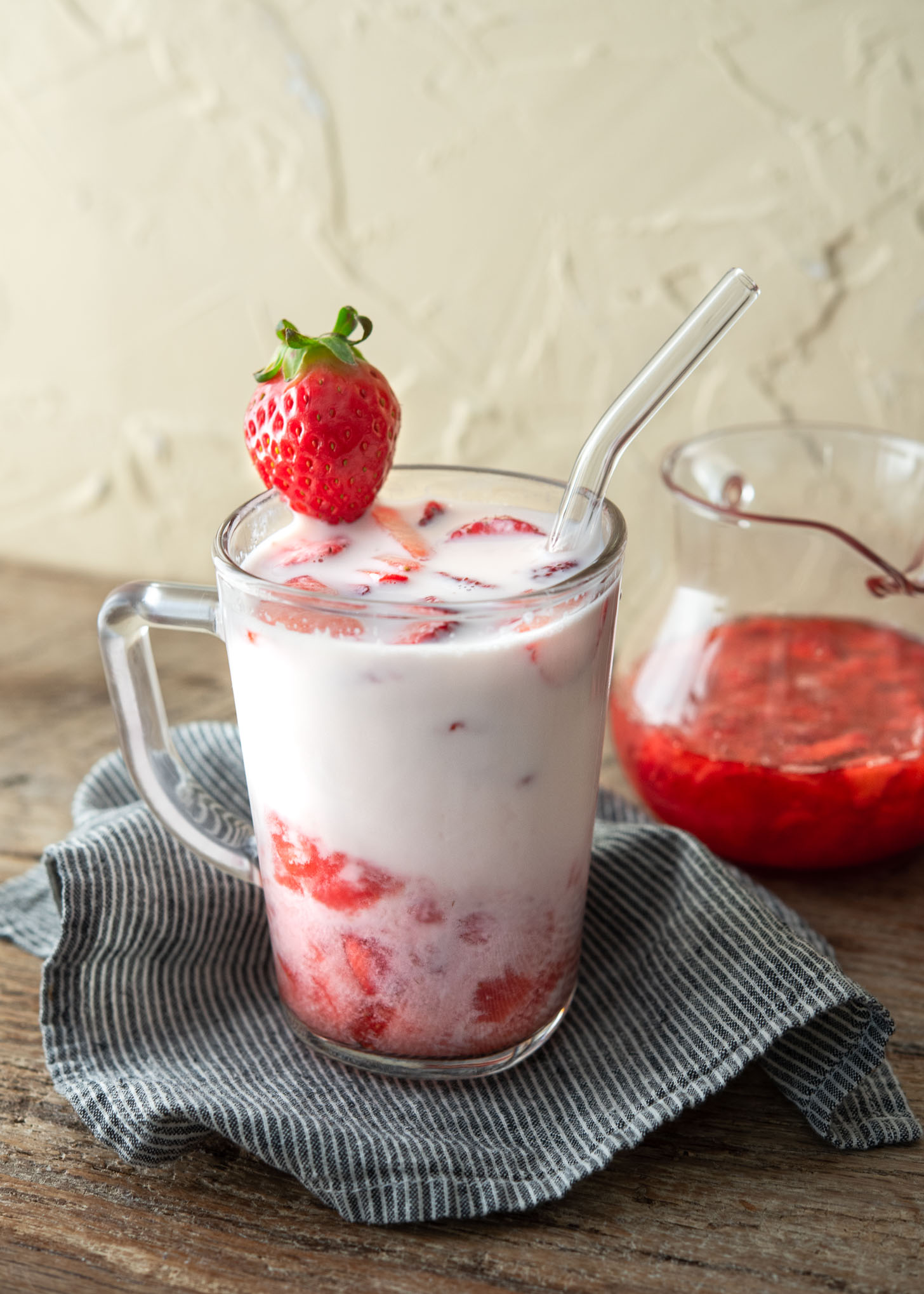 Homemade strawberry syrup marbled with milk in a glass cup garnished with fresh strawberry pieces.