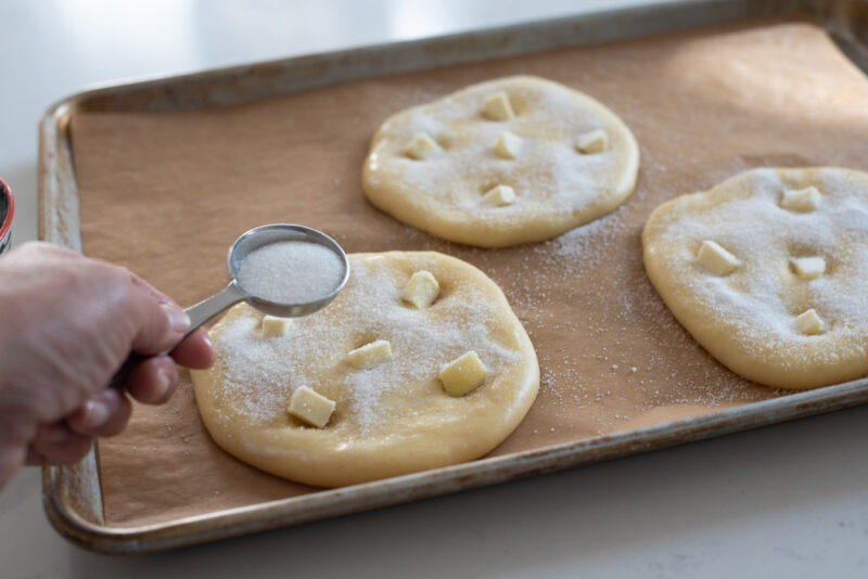 Butter pieces are added to the indentation and a spoonful of sugar is sprinkled over the dough.