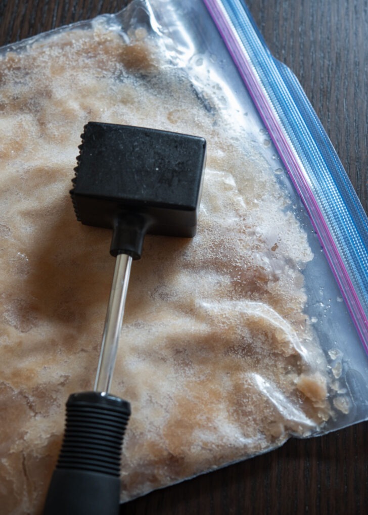 A meat hammer is breaking up the frozen cinnamon ice in a zip bag.