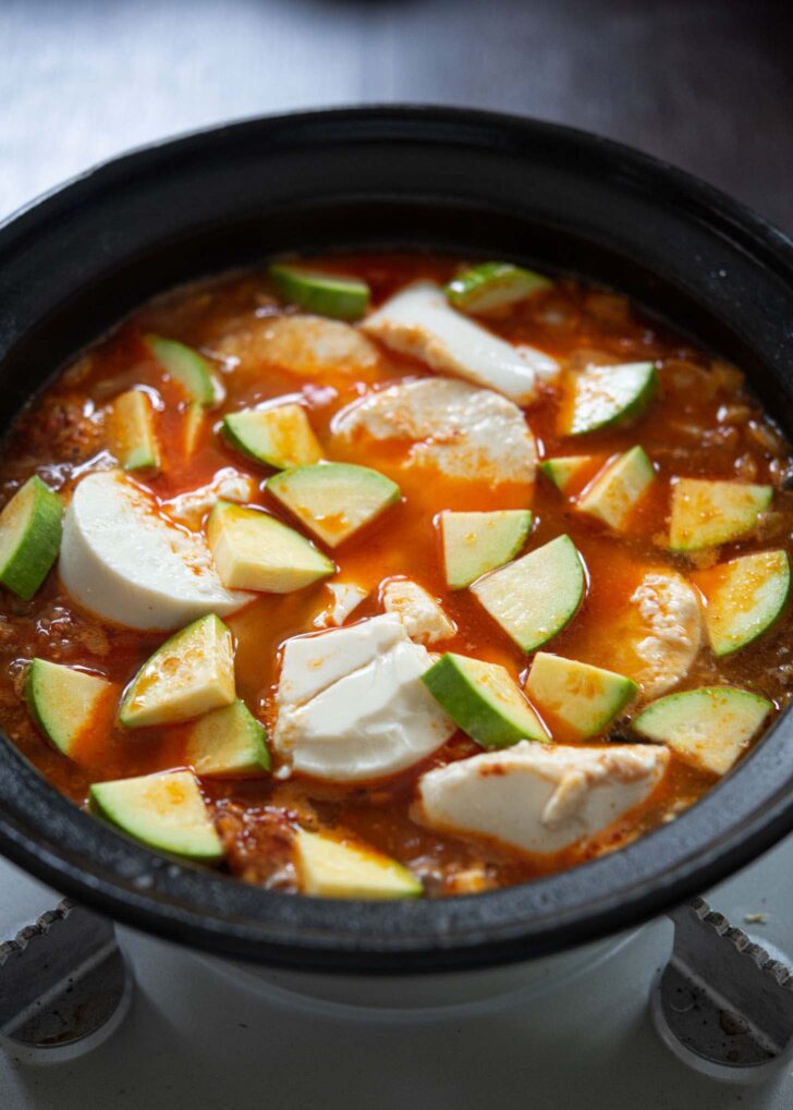 Zucchini slices added to Korean tofu soup in a pot.